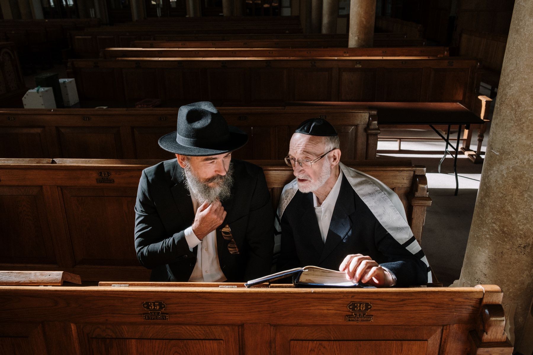 Two men studying a book together in a synagogue pew